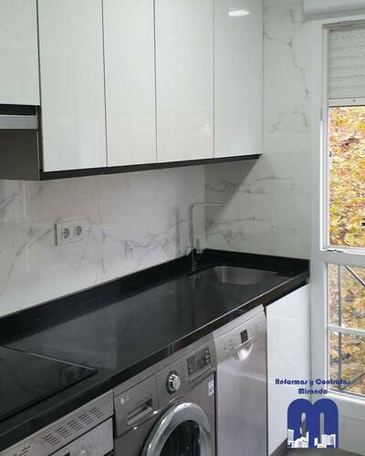 Cocina reformada con distribución lineal, mobiliario blanco, encimera negra y acabados elegantes