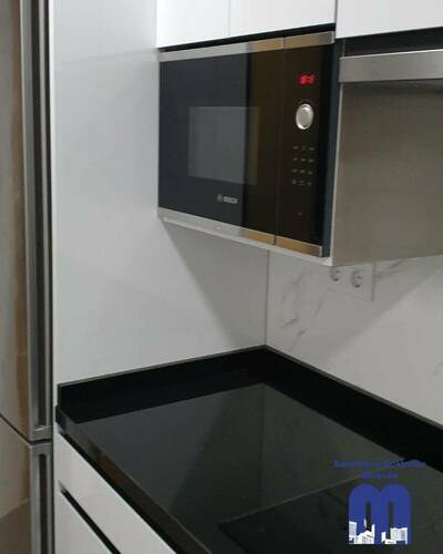 Cocina reformada con distribución lineal, mobiliario blanco, encimera negra y acabados elegantes