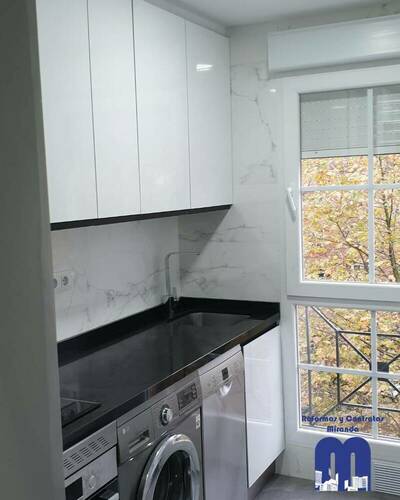Cocina reformada con distribución lineal, mobiliario blanco, encimera negra y acabados elegantes