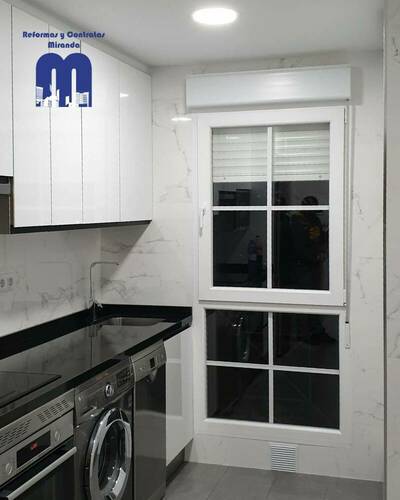 Cocina reformada con distribución lineal, mobiliario blanco, encimera negra y acabados elegantes