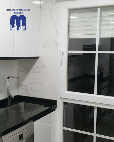 Cocina reformada con distribución lineal, mobiliario blanco, encimera negra y acabados elegantes