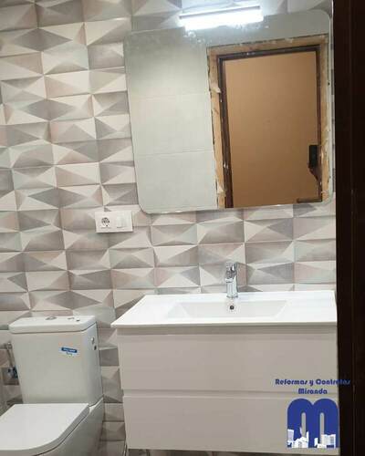 Baño reformado con diseño actual, revestimiento geométrico, ducha con mampara de cristal y mobiliario suspendido, pensado para ofrecer funcionalidad, luminosidad y un estilo contemporáneo.