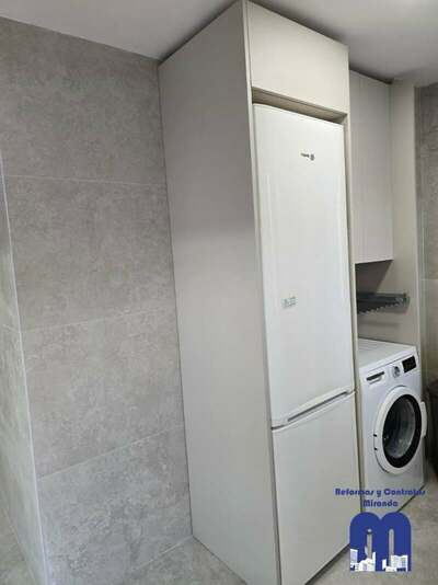 Reforma integral de cocina y cuarto de lavandería en Gijón con azulejo de gran formato, muebles en acabado madera y color viola, techos de pladur e iluminación LED integrada.