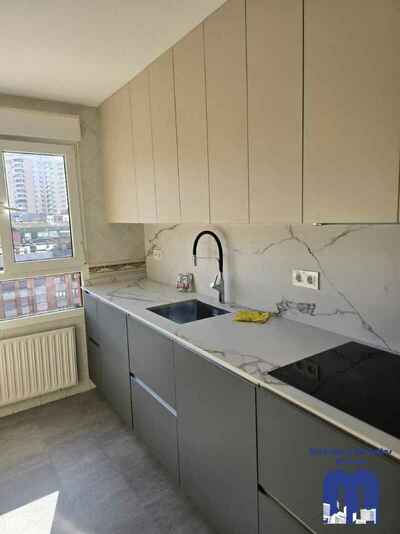 Reforma integral de cocina moderna con mobiliario en acabado tacto seda Fenix verde comodoro y beige, encimera y frente porcelánico Coverlam imitación mármol, suelo vinilico gris, fregadero bajo encimera y grifo monomando flexible de color negro.