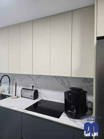 Reforma integral de cocina moderna con mobiliario en acabado tacto seda Fenix verde comodoro y beige, encimera y frente porcelánico Coverlam imitación mármol, suelo vinilico gris, fregadero bajo encimera y grifo monomando flexible de color negro.