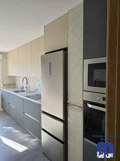 Reforma integral de cocina moderna con mobiliario en acabado tacto seda Fenix verde comodoro y beige, encimera y frente porcelánico Coverlam imitación mármol, suelo vinilico gris, fregadero bajo encimera y grifo monomando flexible de color negro.