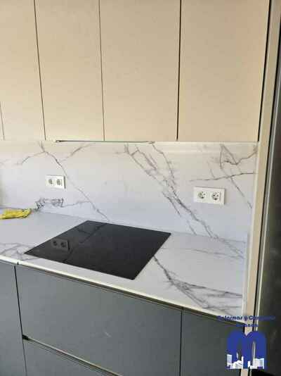 Reforma integral de cocina moderna con mobiliario en acabado tacto seda Fenix verde comodoro y beige, encimera y frente porcelánico Coverlam imitación mármol, suelo vinilico gris, fregadero bajo encimera y grifo monomando flexible de color negro.