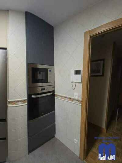 Reforma integral de cocina moderna con mobiliario en acabado tacto seda Fenix verde comodoro y beige, encimera y frente porcelánico Coverlam imitación mármol, suelo vinilico gris, fregadero bajo encimera y grifo monomando flexible de color negro.
